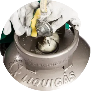 Botijão de gás Liquigás sendo instalado por profissional uniformizado, com utilização da esponja para verificar se há vazamento.
