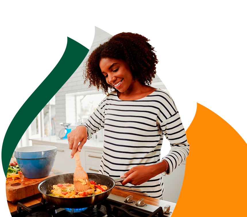 Mulher sorridente cozinhando em fogão com chama azul acesa.
